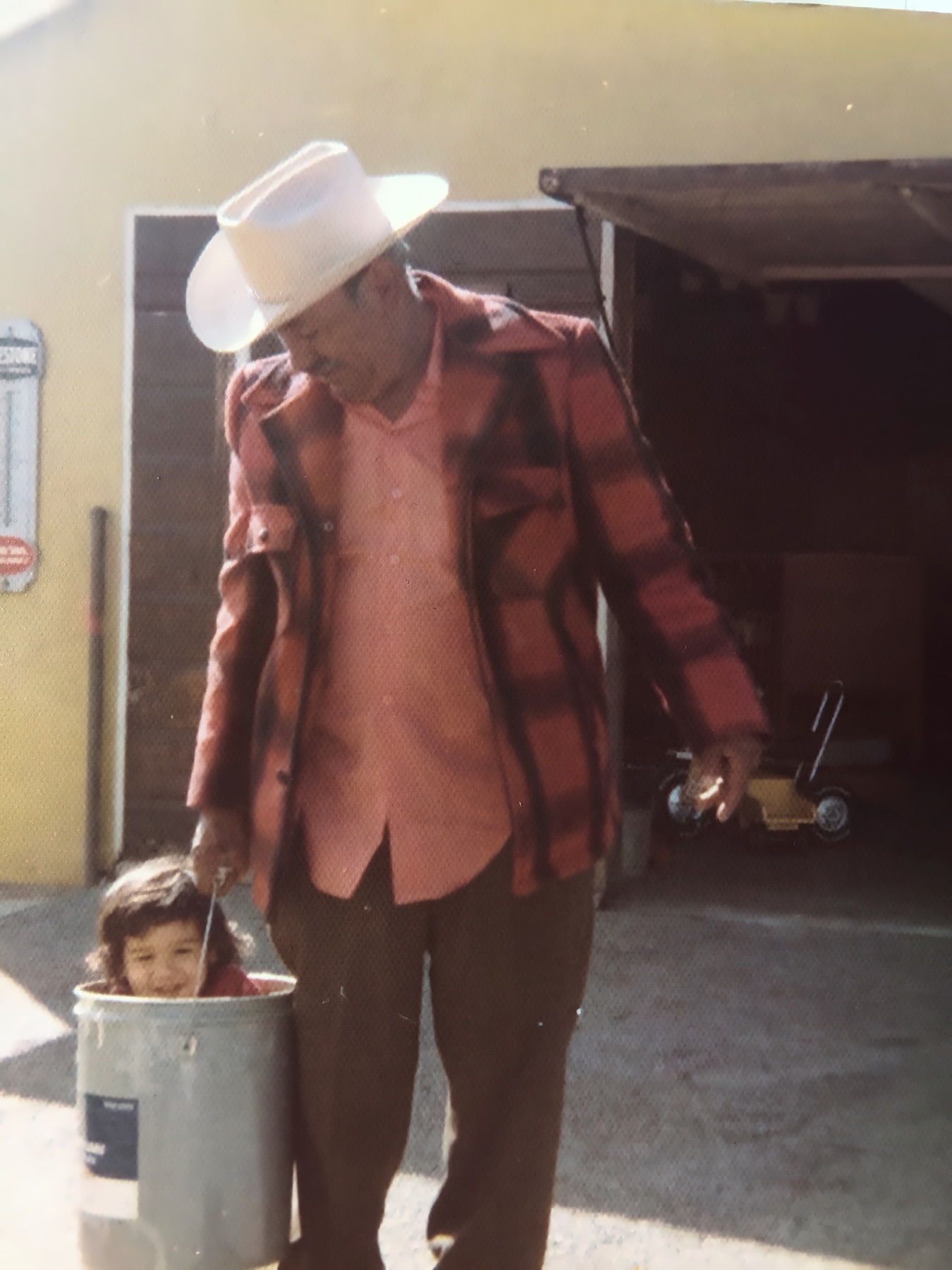 Chepé in a white cowboy hat carrying young Martin inside a metal bucket in 1976.