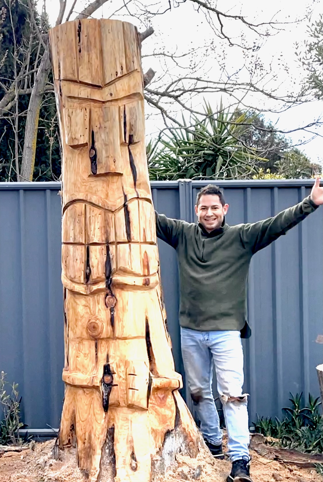 Martin standing beside the completed tall wooden carving of Tāne Mahuta