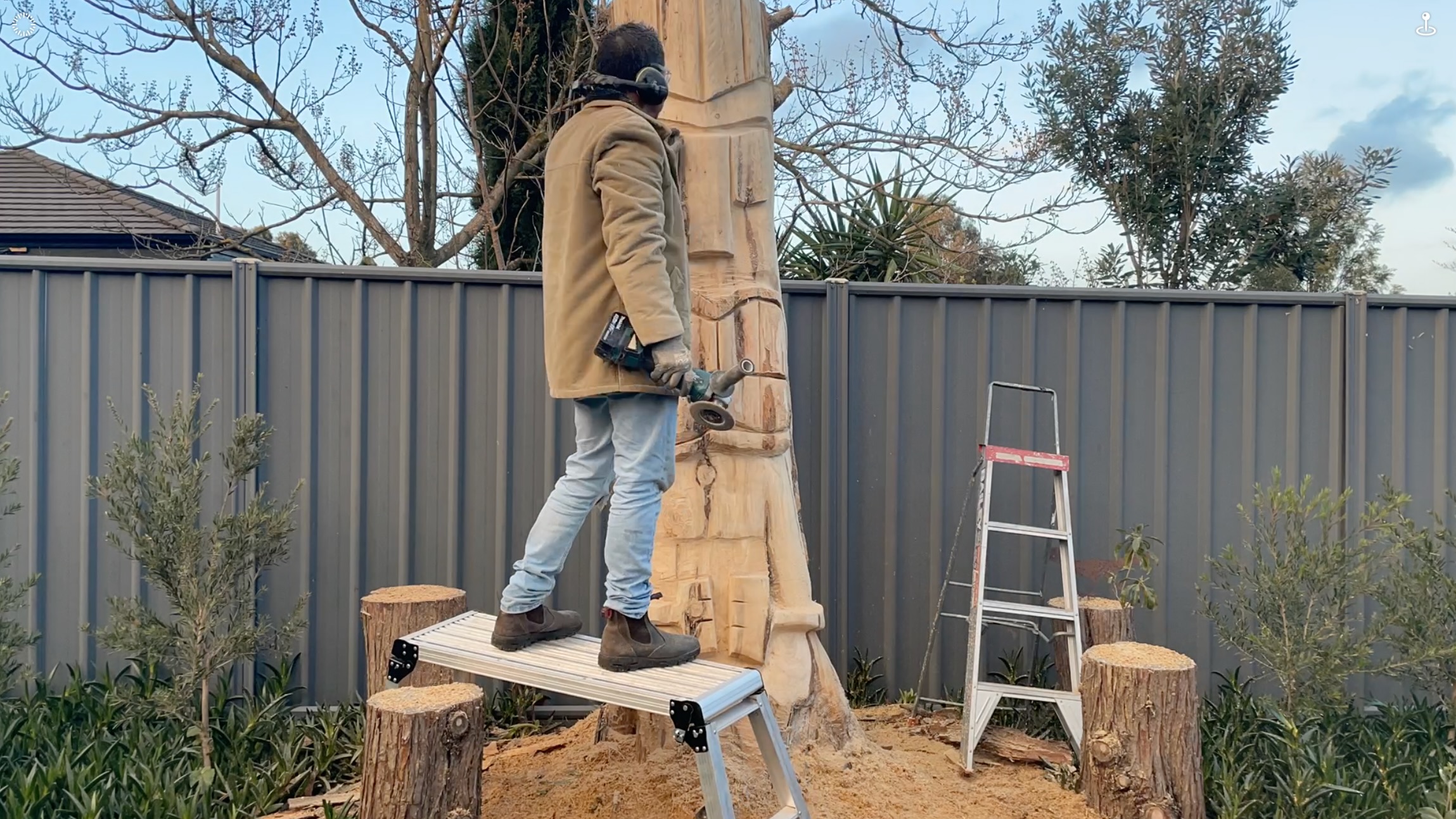 Martin carving the tall wooden figure of Tāne Mahuta outdoors with an angle grinder.