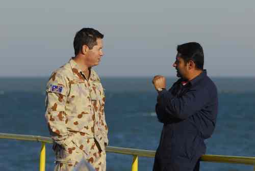 Two men speaking on the deck of the KAAOT oil terminal with the Persian Gulf behind them.